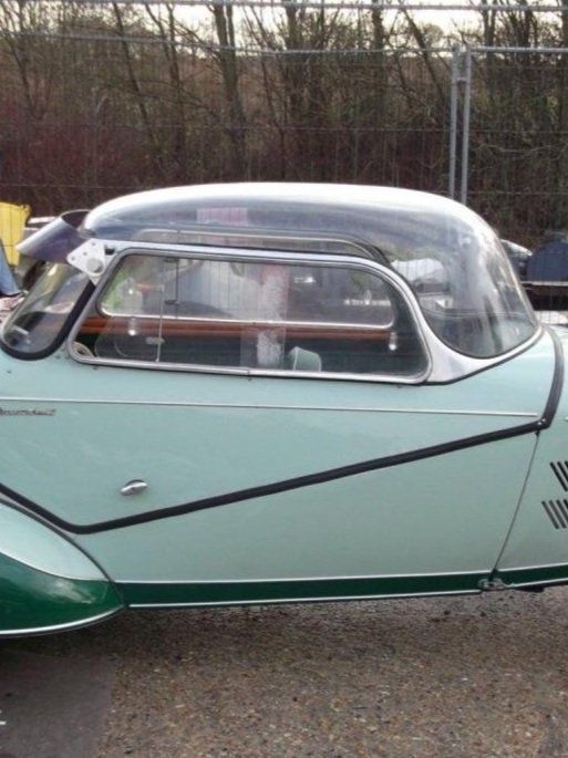 Vintage mint-green and white streamlined car with a clear bubble roof, parked outdoors.