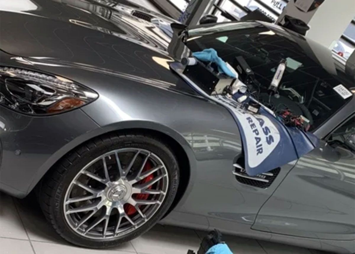 Gray sports car with hood open in a garage, showing a large front wheel and red brake caliper
