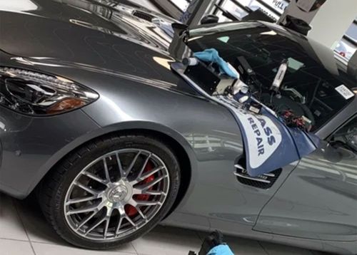 Gray sports car with hood open in a garage, showing a large front wheel and red brake caliper