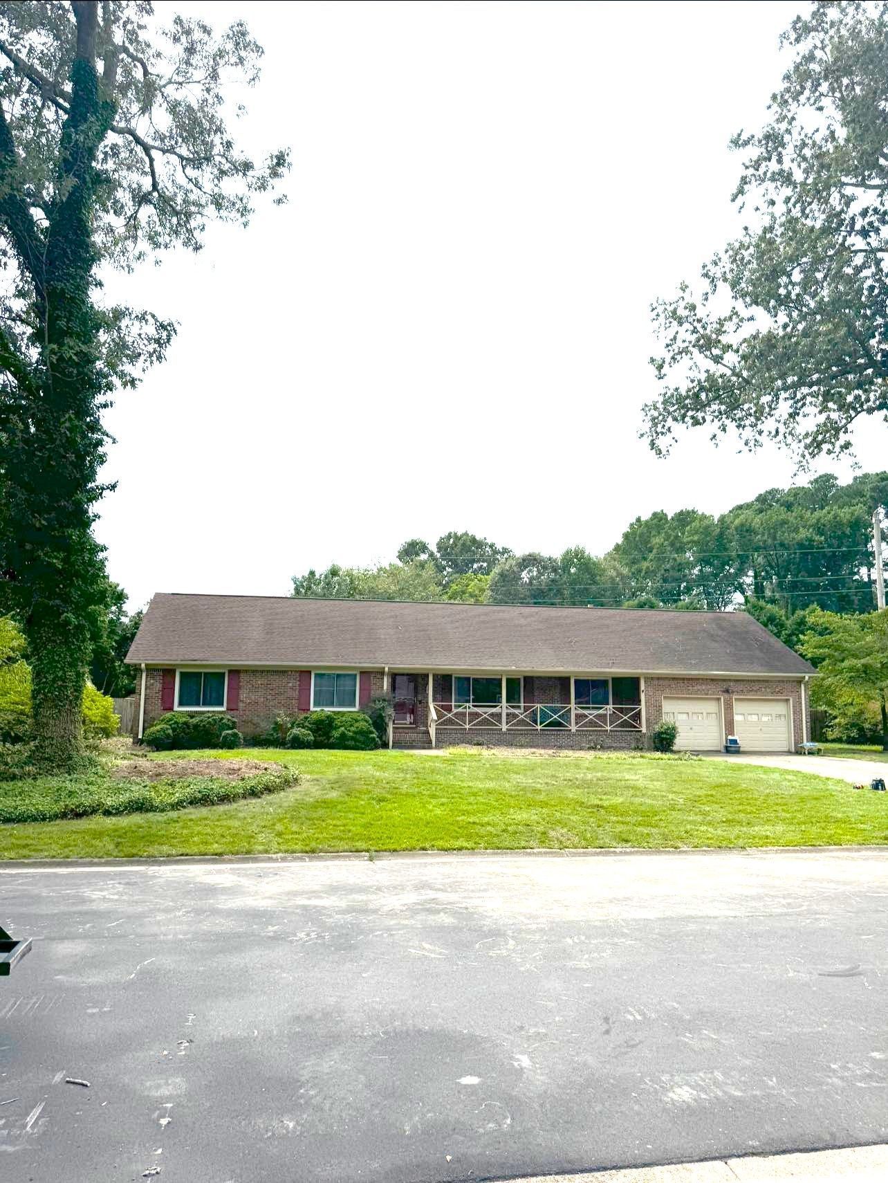 Single-story brick house with a large front lawn and driveway under trees