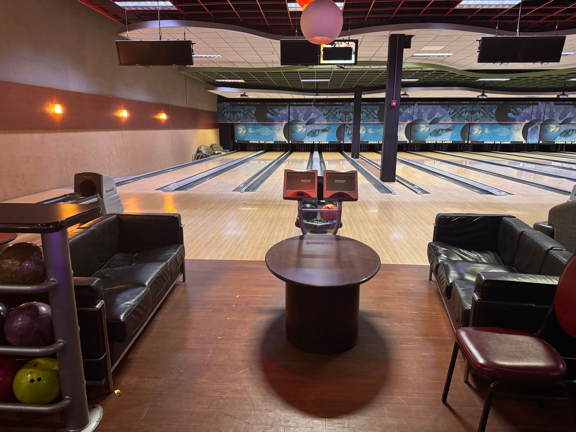 Bowling alley seating area with leather couches, a round table, and lanes stretching into the distance