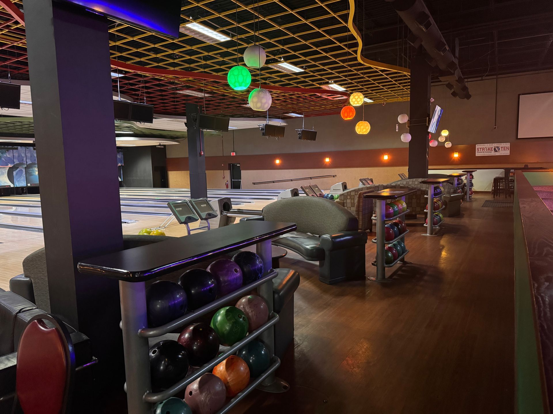 Indoor bowling alley with lit lanes, colorful hanging lights, and ball racks in the foreground