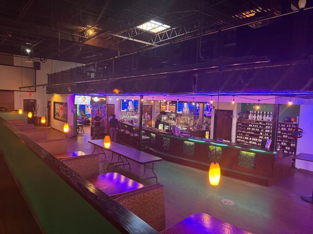 Nightclub interior with purple and blue lights, a bar, and glowing lanterns on a walkway