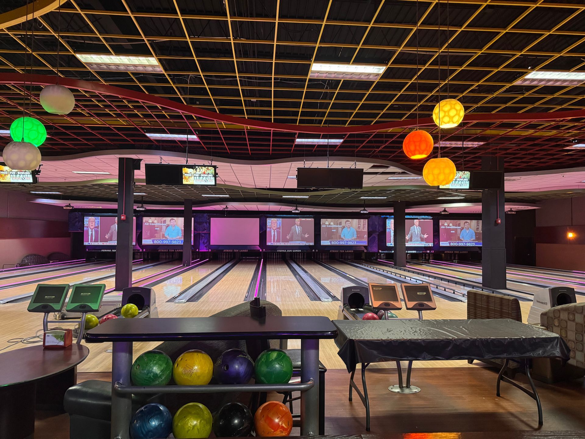 Bowling alley with colorful hanging lights, empty lanes, and ball racks in the foreground