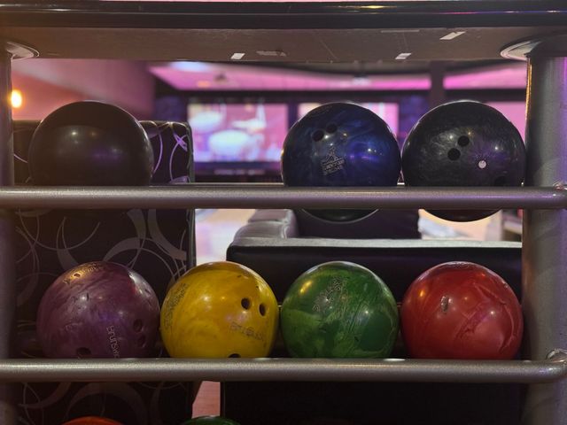 Bowling balls lined on a rack in a bowling alley, with colorful balls in the foreground.