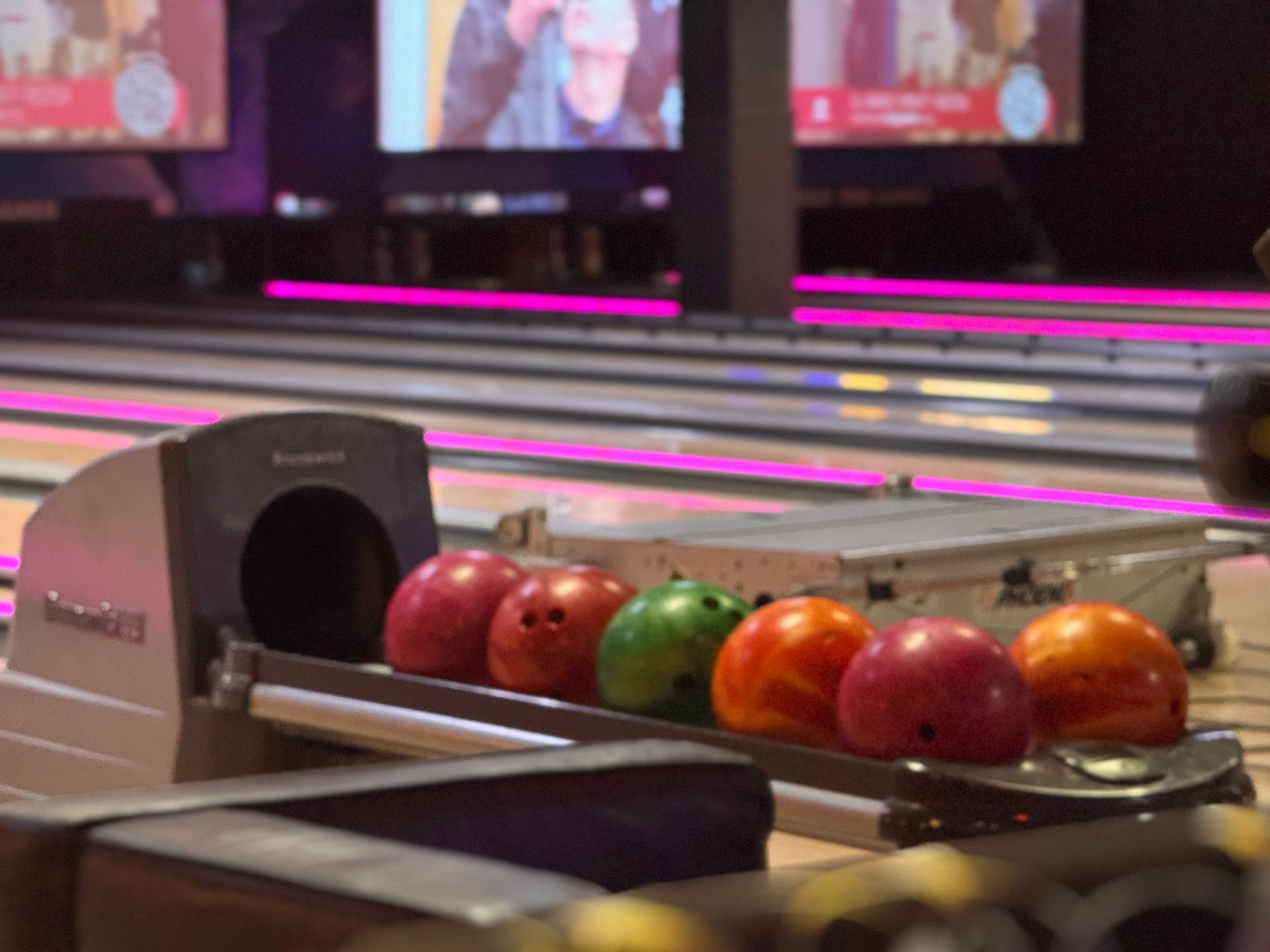 Bowling lane with a ball return holding several colorful bowling balls in a neon-lit alley