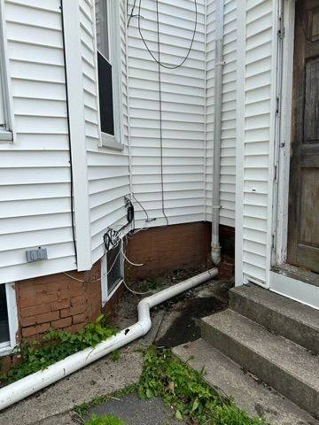 Exterior corner of a white-sided building with a downspout and white drainage pipe on ground; concrete steps.