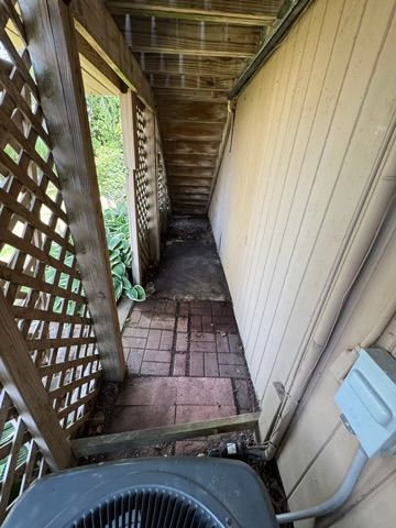 Narrow outdoor walkway with brick flooring and lattice on one side, air conditioning unit at the bottom.