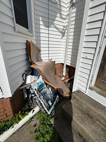 Pile of discarded items, including wood and posters, next to a white house with steps.
