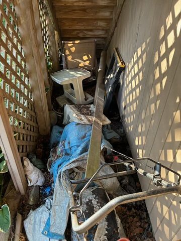 Narrow outdoor space filled with debris: table, metal parts, blue tarp, and wood latticework.