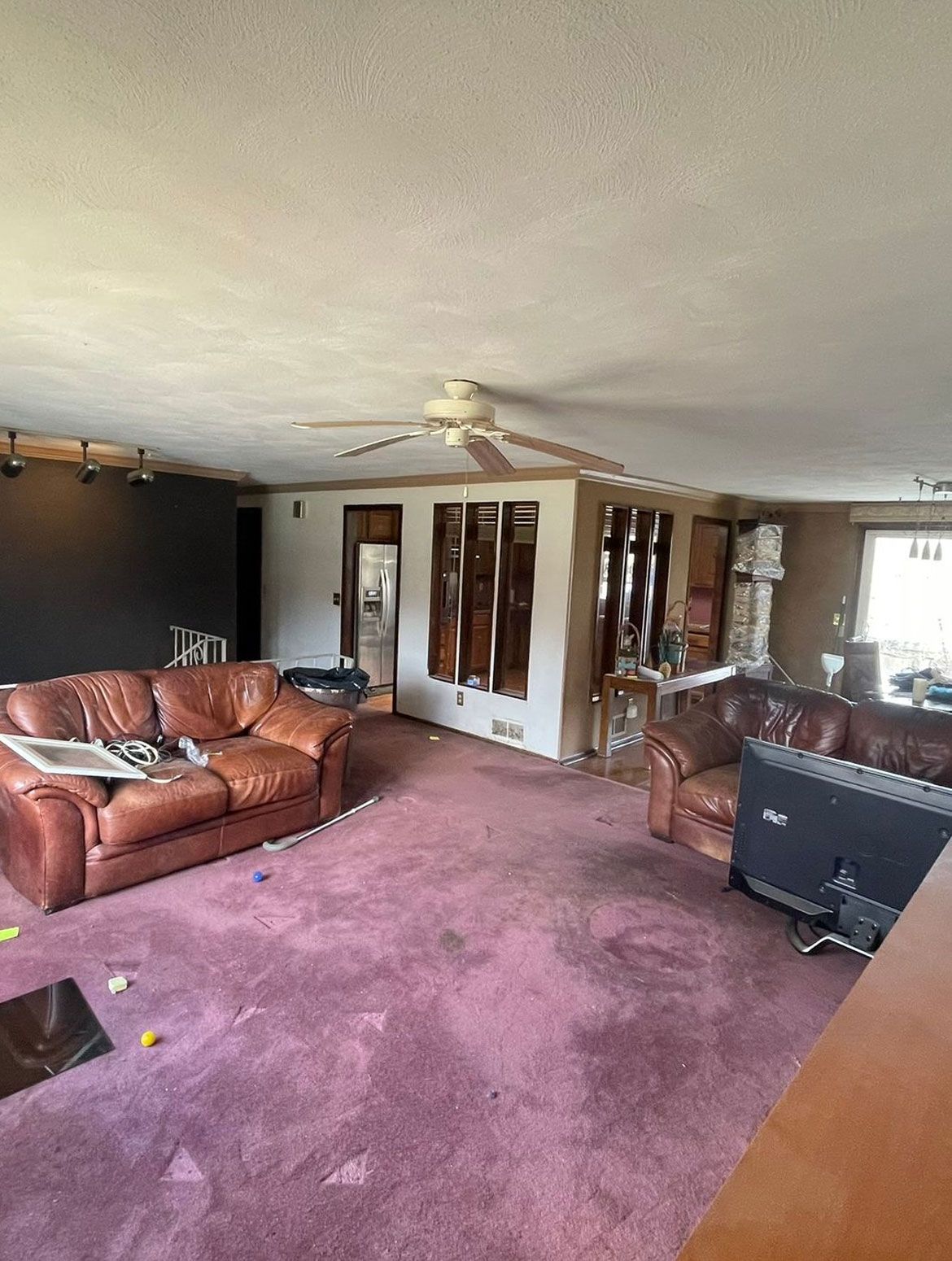 A living room with a couch , chairs , a television and a ceiling fan.