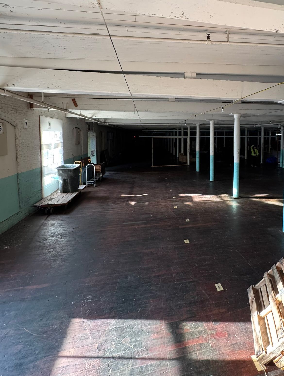 Empty, dark warehouse interior with white pillars, a dark floor, and stacks of pallets.