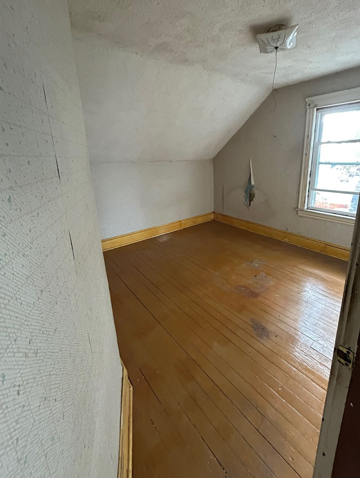 Small attic room with wood floor, sloped ceiling, small window.
