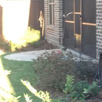 A brick house with a screened in porch and a lawn in front of it.