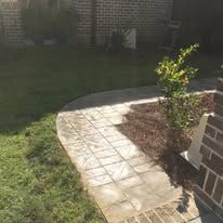 A brick walkway leading to a lush green yard next to a brick building.