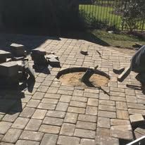 A person is laying bricks on a patio.