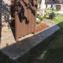 A wooden fence is sitting next to a brick walkway in front of a house.