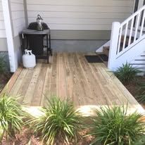 A wooden deck next to a house with stairs and a propane tank.