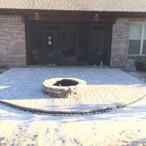 A fire pit is sitting on a patio in front of a brick house.