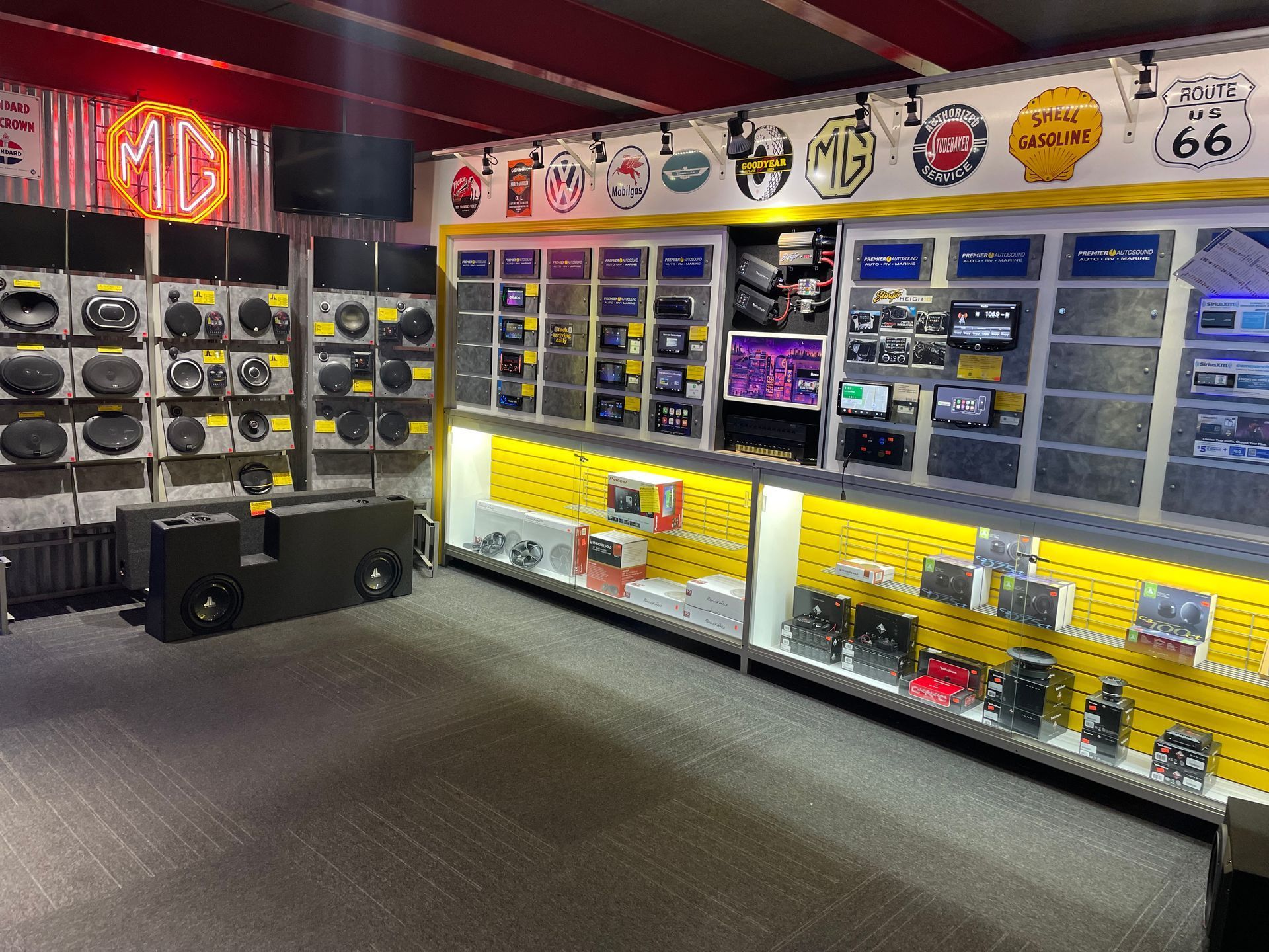 An indoor display of car audio equipment, including speakers, subwoofers, and head units on shelves with yellow pegboard.