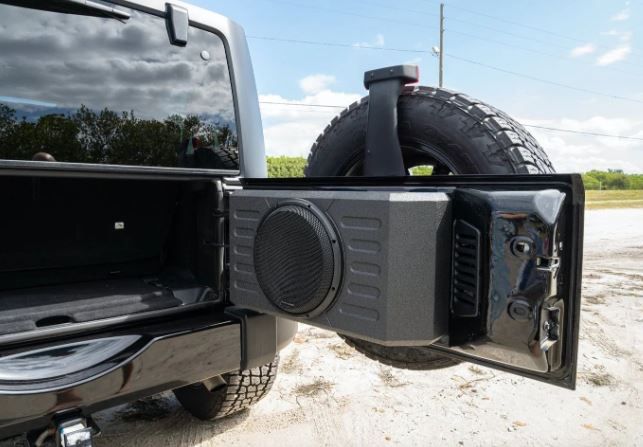 Black Jeep's open rear door with a speaker, holding a large tire