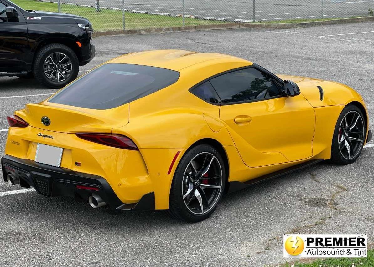 A bright yellow Toyota Supra coupe parked in an outdoor lot, viewed from the rear three-quarter angle.