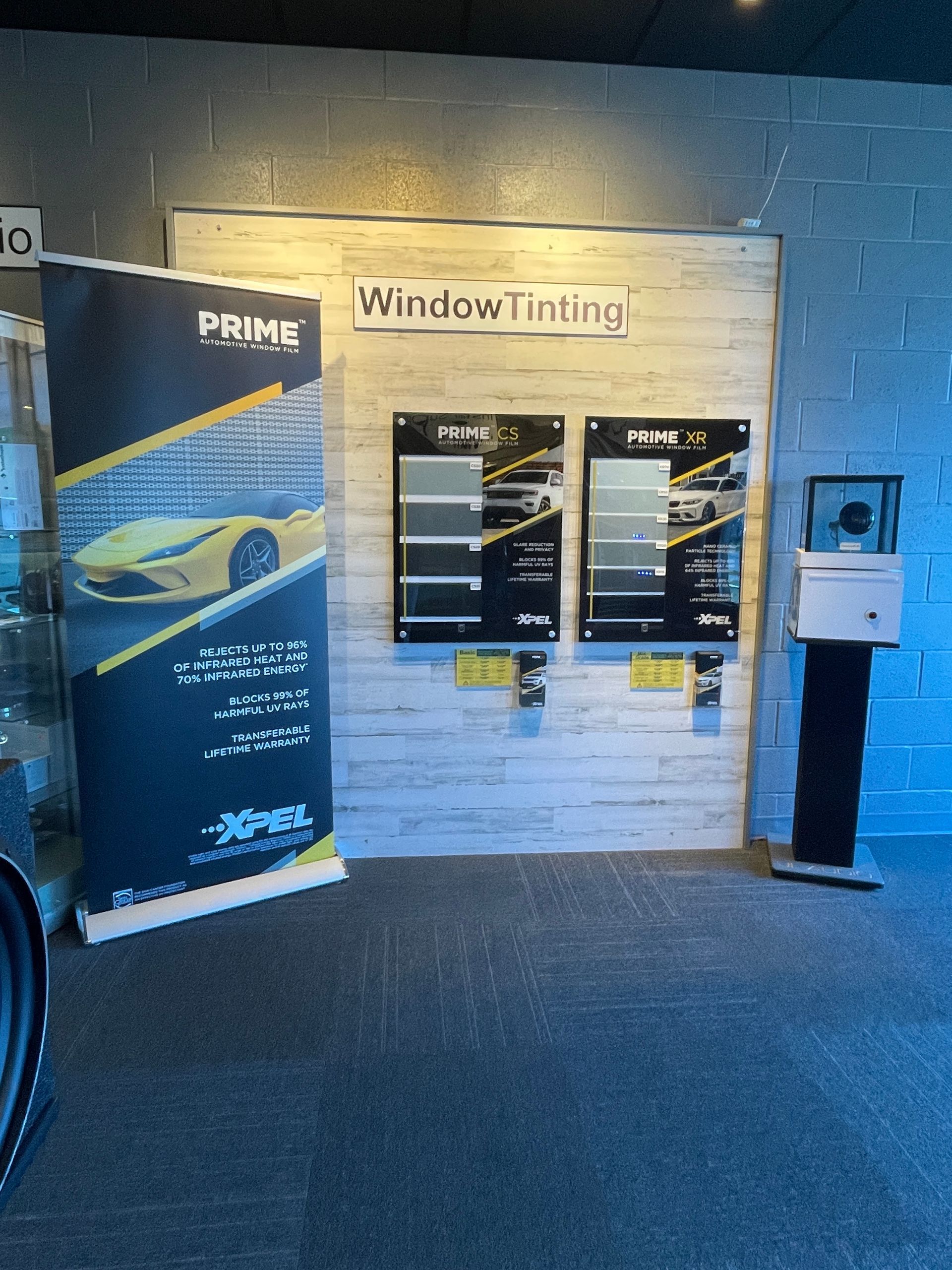 A professional display of automotive window tinting films, featuring brand signage and product samples on a wood wall.