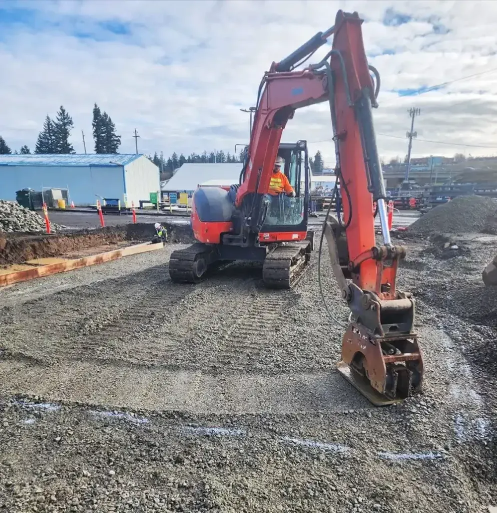 A red and orange excavator is working on a gravel road.