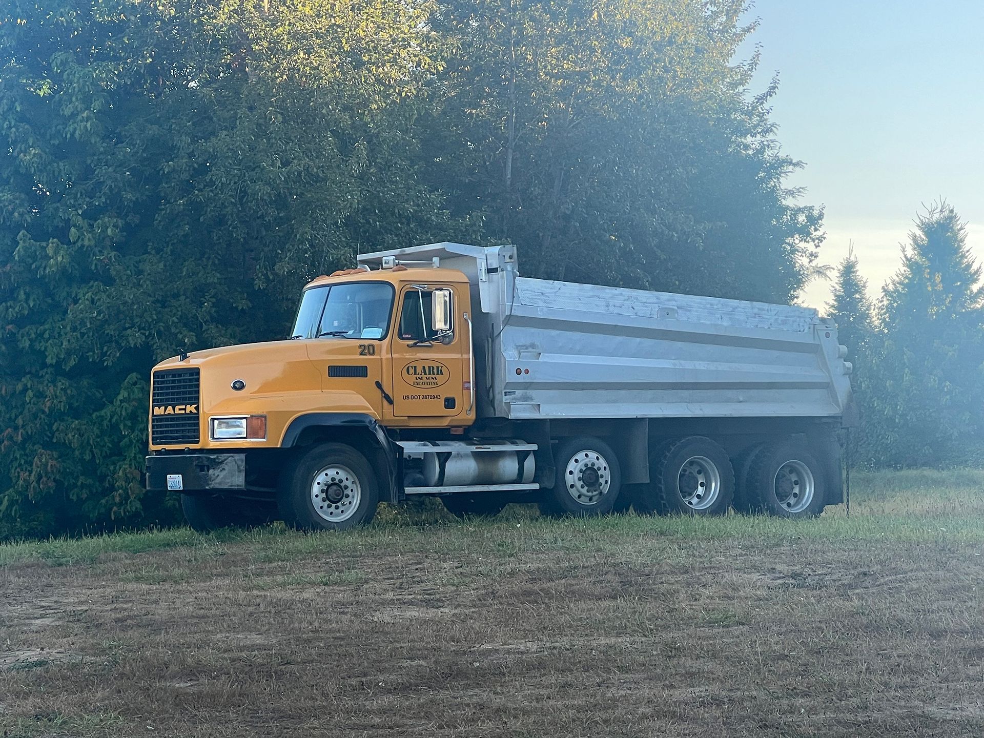 A yellow dump truck is parked in a field with trees in the background.