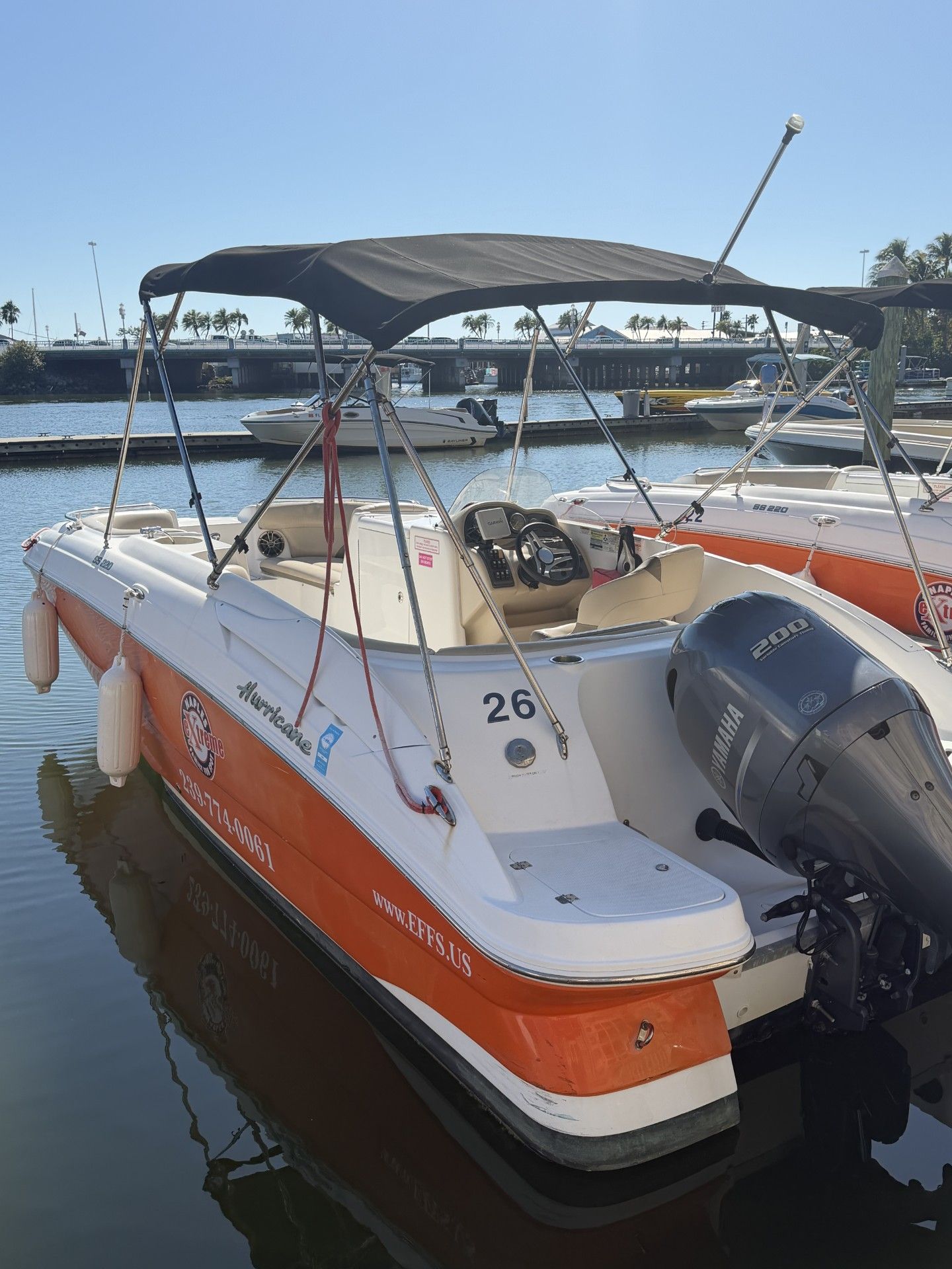 Boat with orange and white accents at a dock, black canopy, and a Yamaha engine. Number 26 is visible.