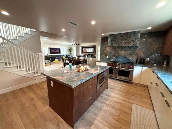 Modern kitchen with granite island, wood floors, white cabinets, and staircase in a bright open-plan home