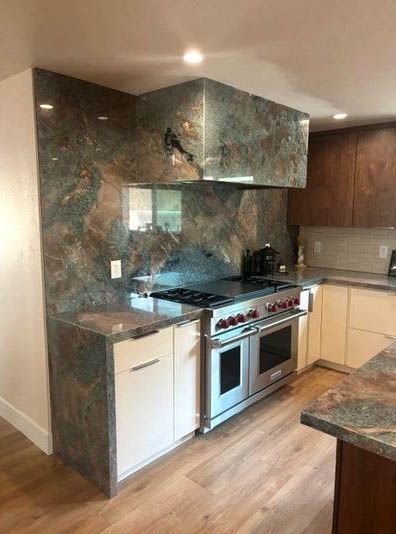 Modern kitchen with dark marble backsplash, white cabinets, stainless steel oven, and wood floors