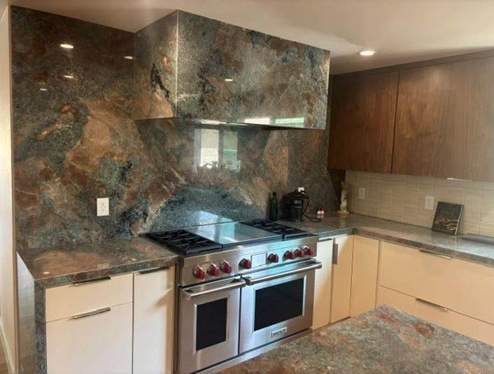 Modern kitchen with stainless steel stove, dark stone backsplash, wood cabinets, and light countertops