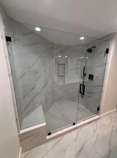 Modern glass shower enclosure with marble-look tile walls and a white tub base.