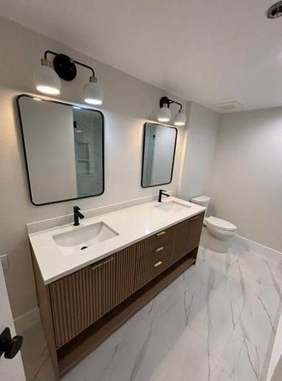 Modern bathroom with double vanity, mirrors, wall sconces, and white marble-style floor.