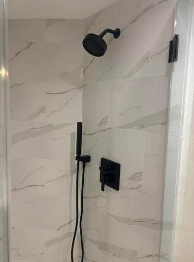 Modern shower with black showerhead and controls against white marble tile wall