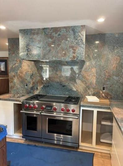 Modern kitchen with stainless steel stove, marble backsplash, and light wood cabinetry