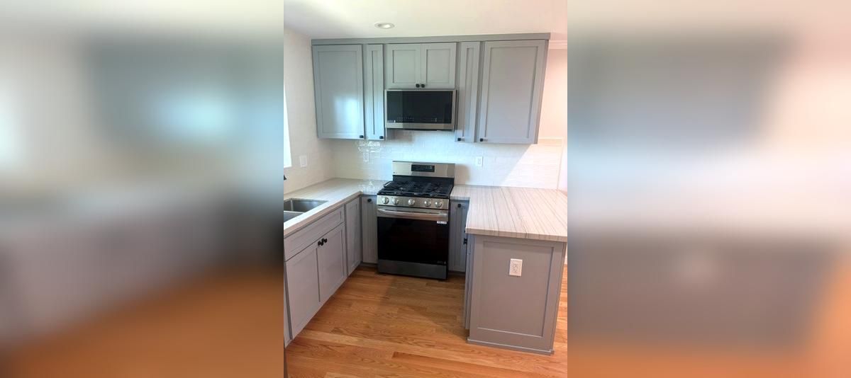 Modern kitchen with white cabinets, stainless stove, black microwave, and wood floor