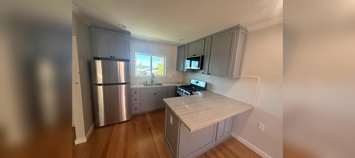 Bright kitchen with stainless fridge, white cabinets, island, and a window above the sink.