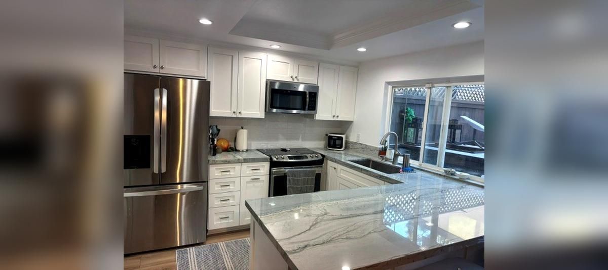 Modern kitchen with stainless steel appliances, white cabinets, marble countertops, and a large island.