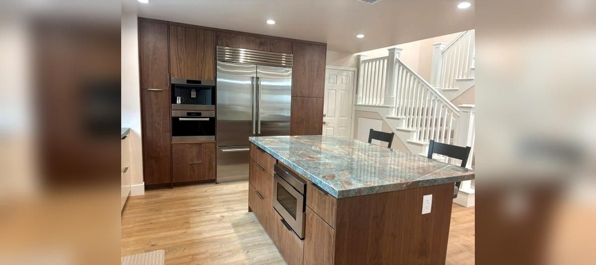 Modern kitchen with wood cabinets, granite island, stainless appliances, and staircase in the background