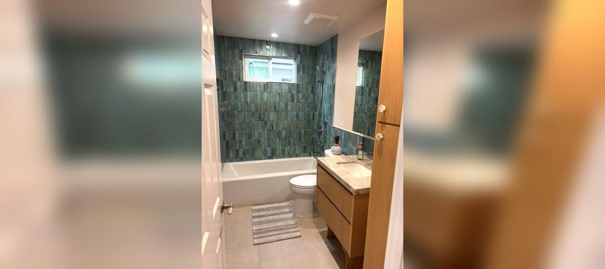 Modern bathroom with a glass shower, patterned green wall, sink vanity, and striped floor mat.