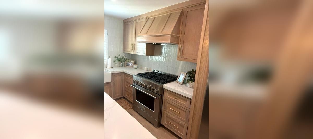 Modern kitchen with light wood cabinets, black stove, white countertops, and stainless sink.