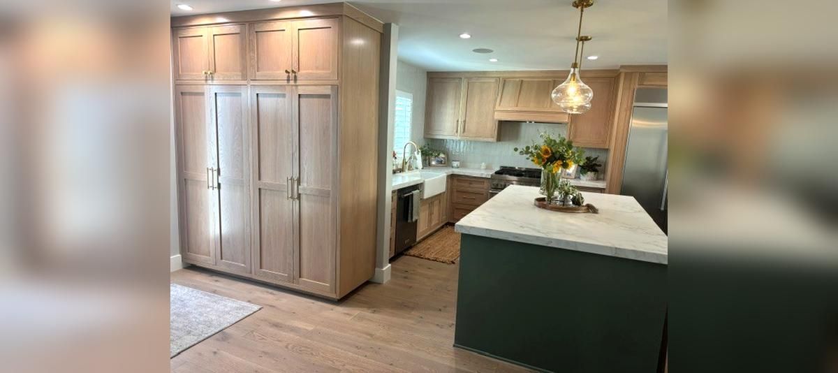 Bright kitchen with stainless steel fridge, white island, and green cabinets, seen from the hallway