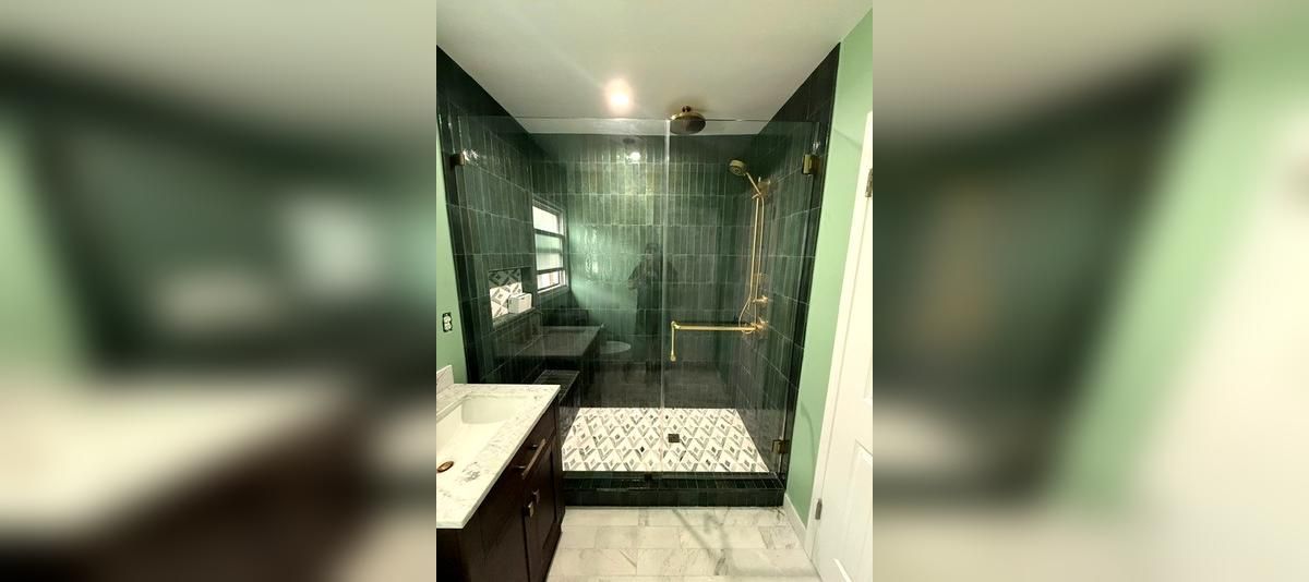 Modern bathroom with a glass-enclosed shower, dark green tile, and a vanity sink.