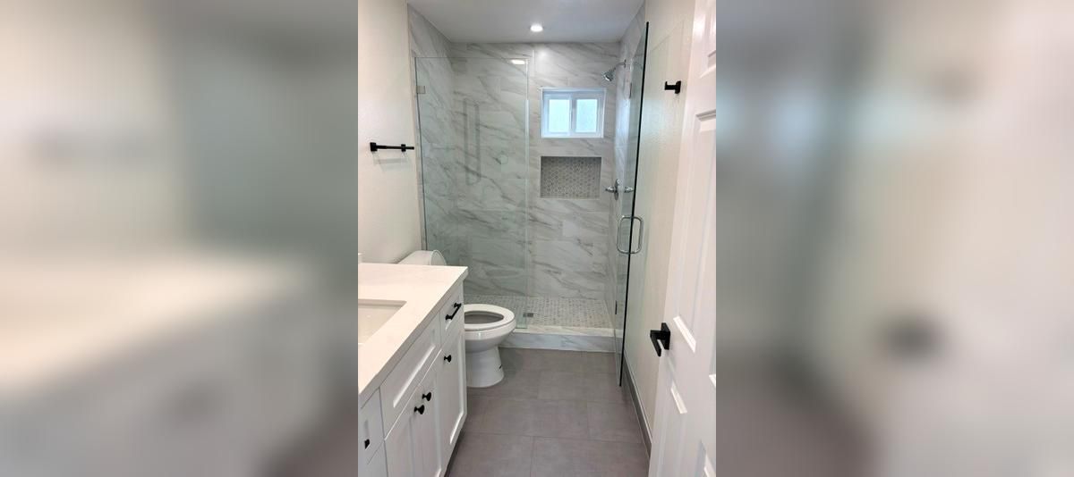 Narrow bathroom with white vanity, toilet, and glass shower tiled in gray stone