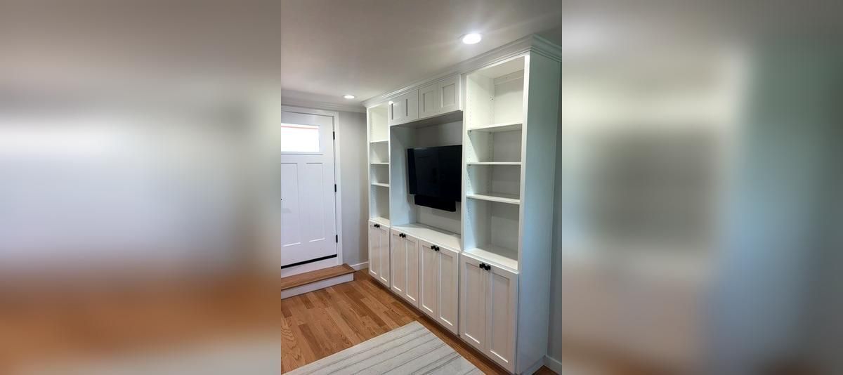 Bright built-in living room wall with TV, white shelves, and cabinets on wood floors