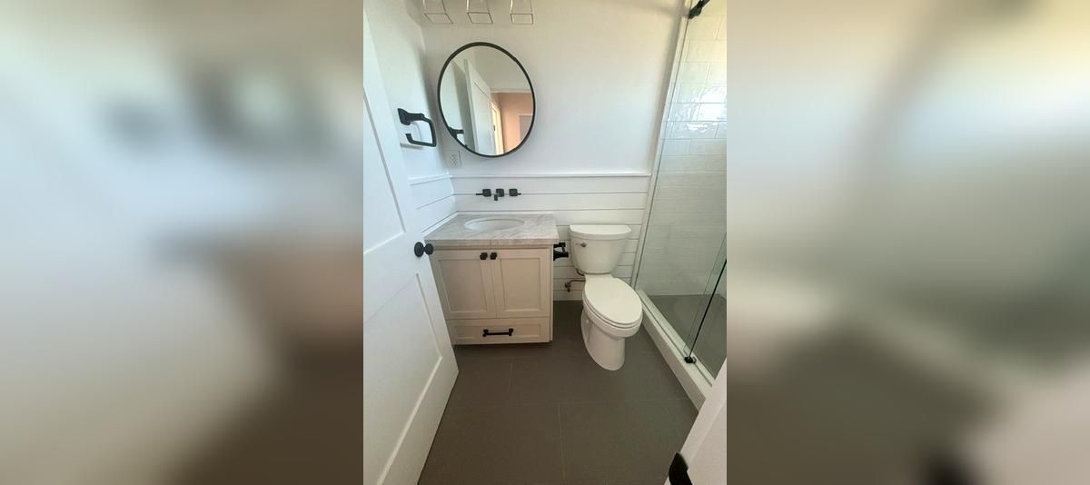 Small white bathroom with a sink, round mirror, toilet, and bathtub with a shower curtain.