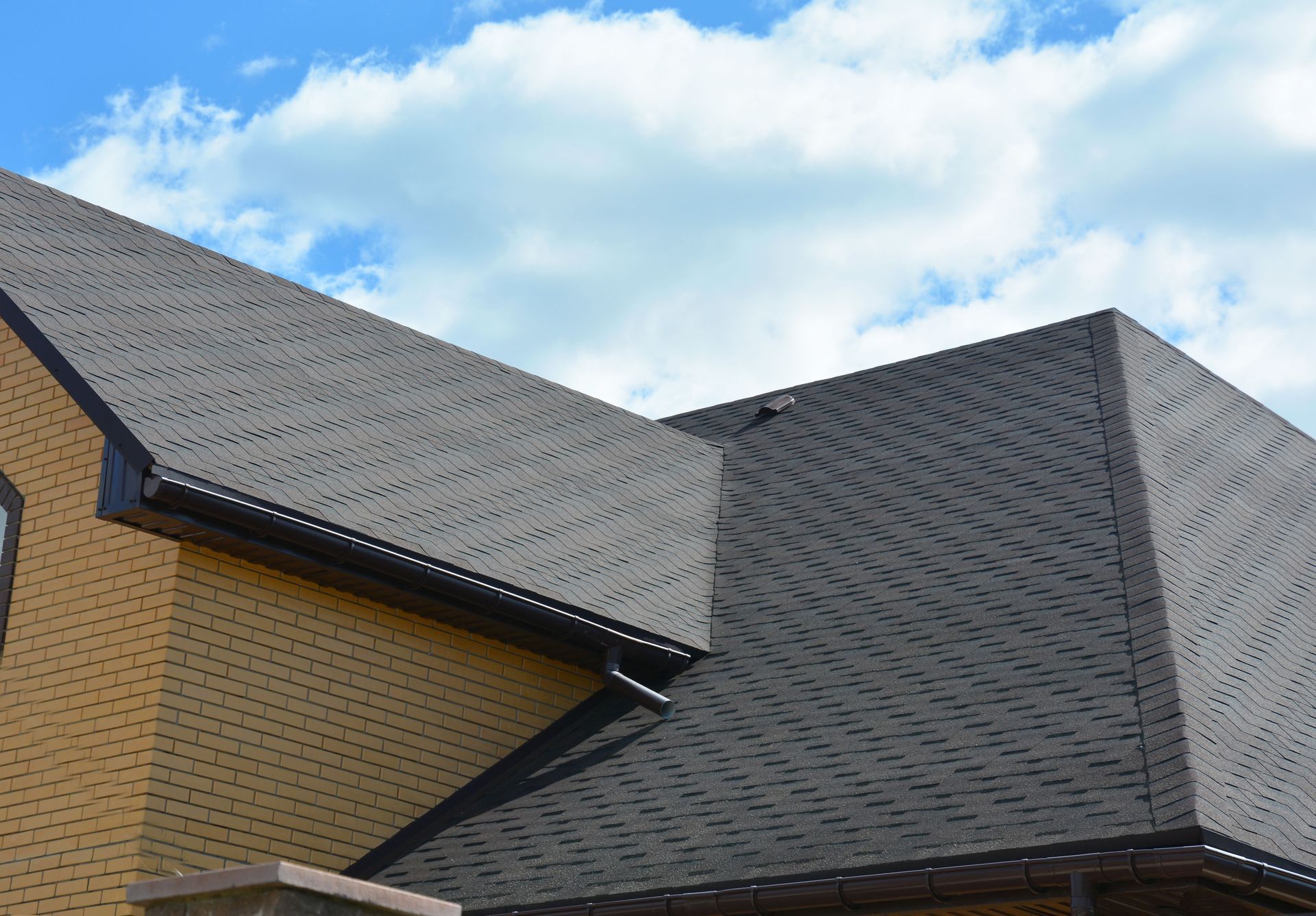 Brick house with a dark, textured roof against a blue sky with clouds.