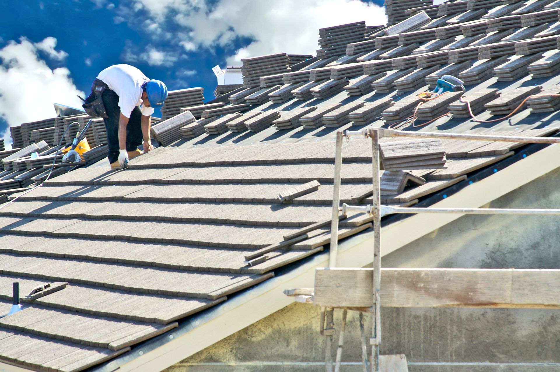 Roofer in hard hat installing roofing tiles on a residential roof; sunny day.